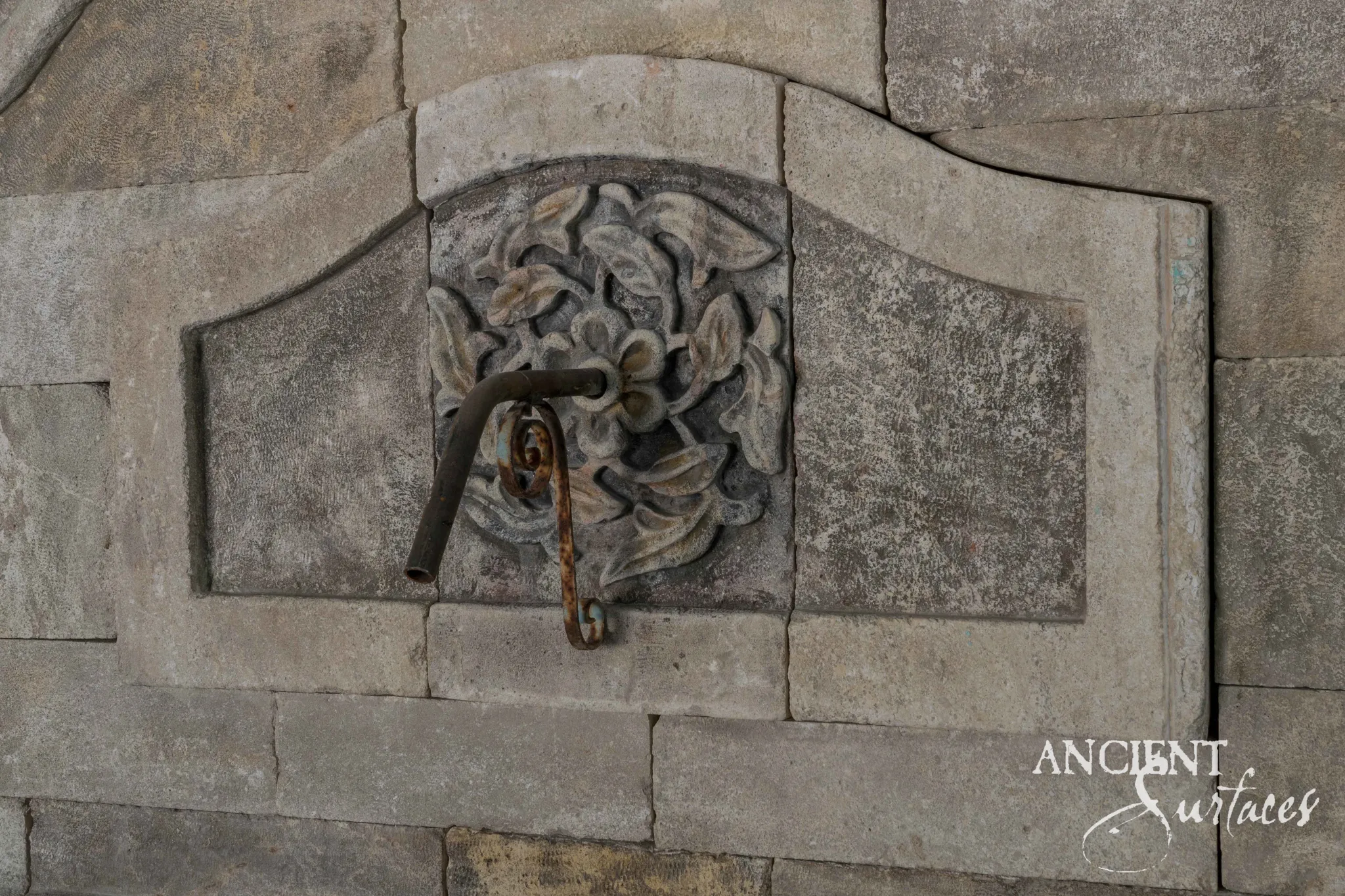Reclaimed antique limestone wall fountain from Ancient Surfaces displayed in an architectural garden setting