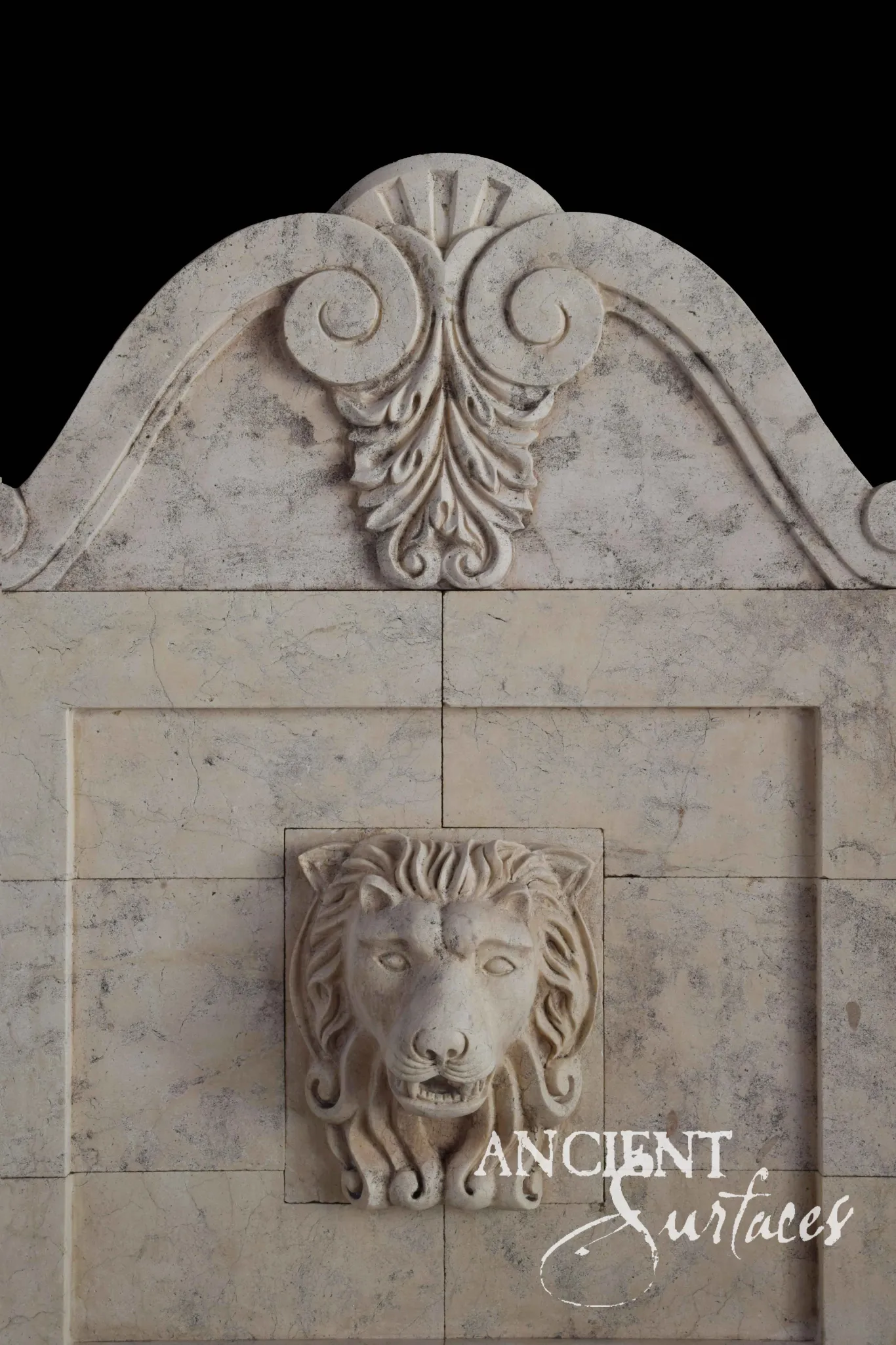 Reclaimed antique limestone wall fountain from Ancient Surfaces with a carved lion mask spout beneath a scroll and acanthus pediment on a marbleized stone panel