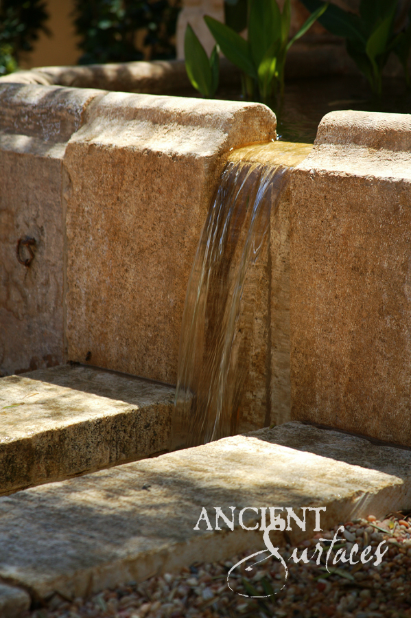 Reclaimed antique limestone step water feature from Ancient Surfaces with water sheeting off stacked stone slabs into a planted garden pond