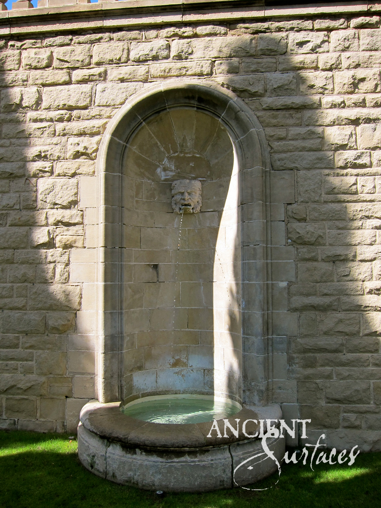Reclaimed antique limestone wall fountain from Ancient Surfaces with a shell like niche, a spiral iron spout and carved scroll volute brackets over a rectangular basin