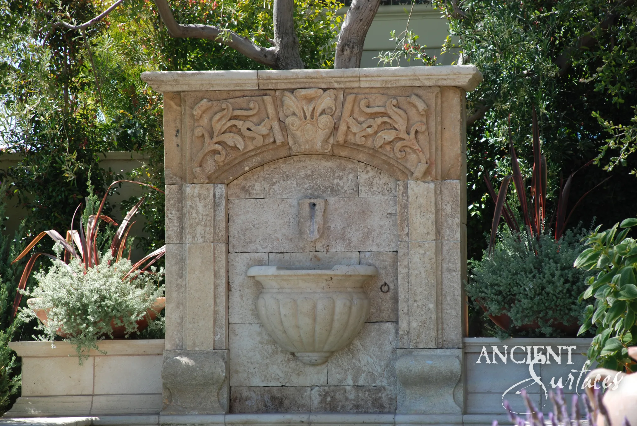 Reclaimed antique limestone wall fountain from Ancient Surfaces carved with a quatrefoil cartouche and scroll brackets over a faceted octagonal basin