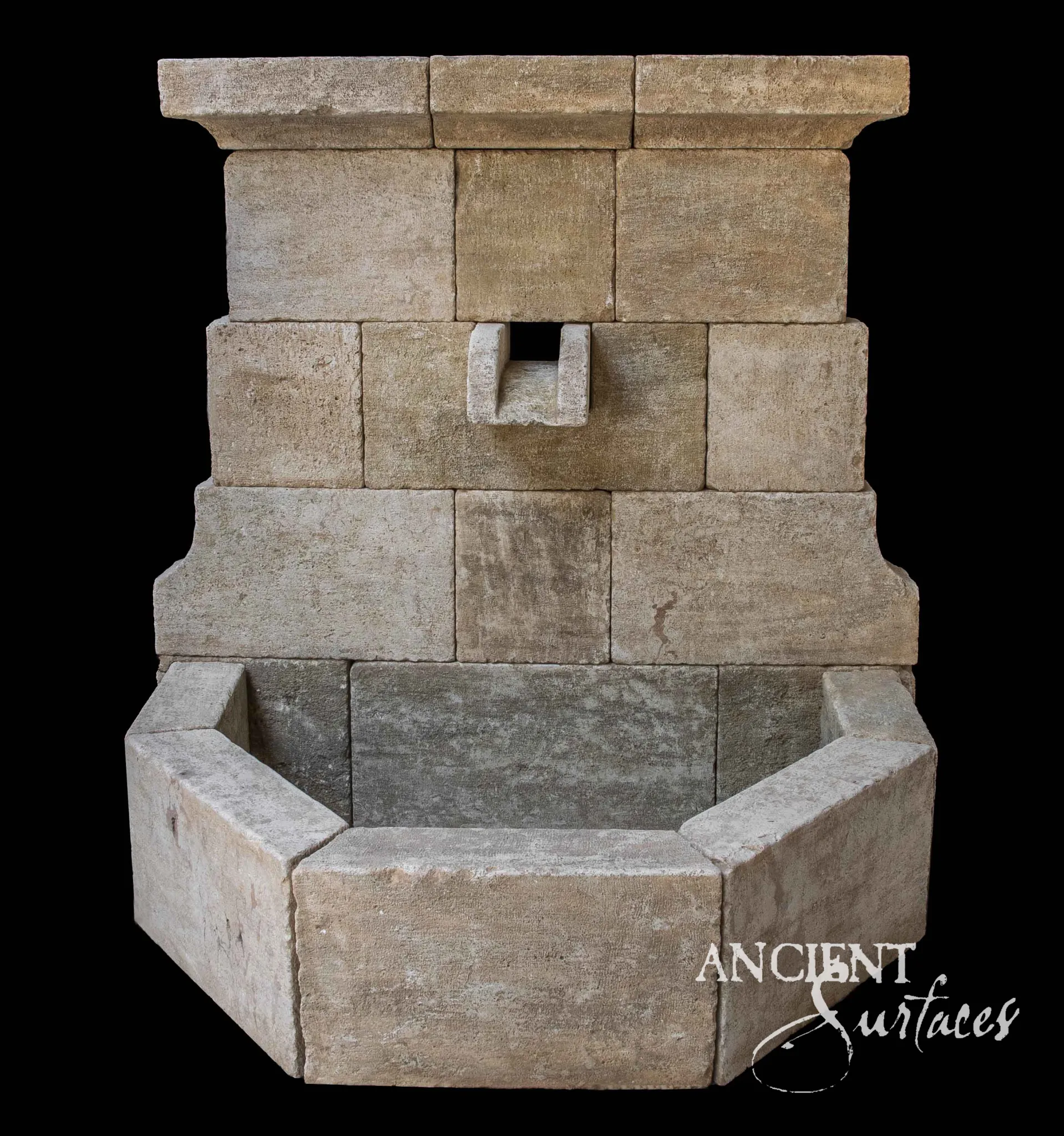 Reclaimed antique limestone wall fountain from Ancient Surfaces with a carved lion mask spout set into a deep rounded arch niche in a rusticated stone wall