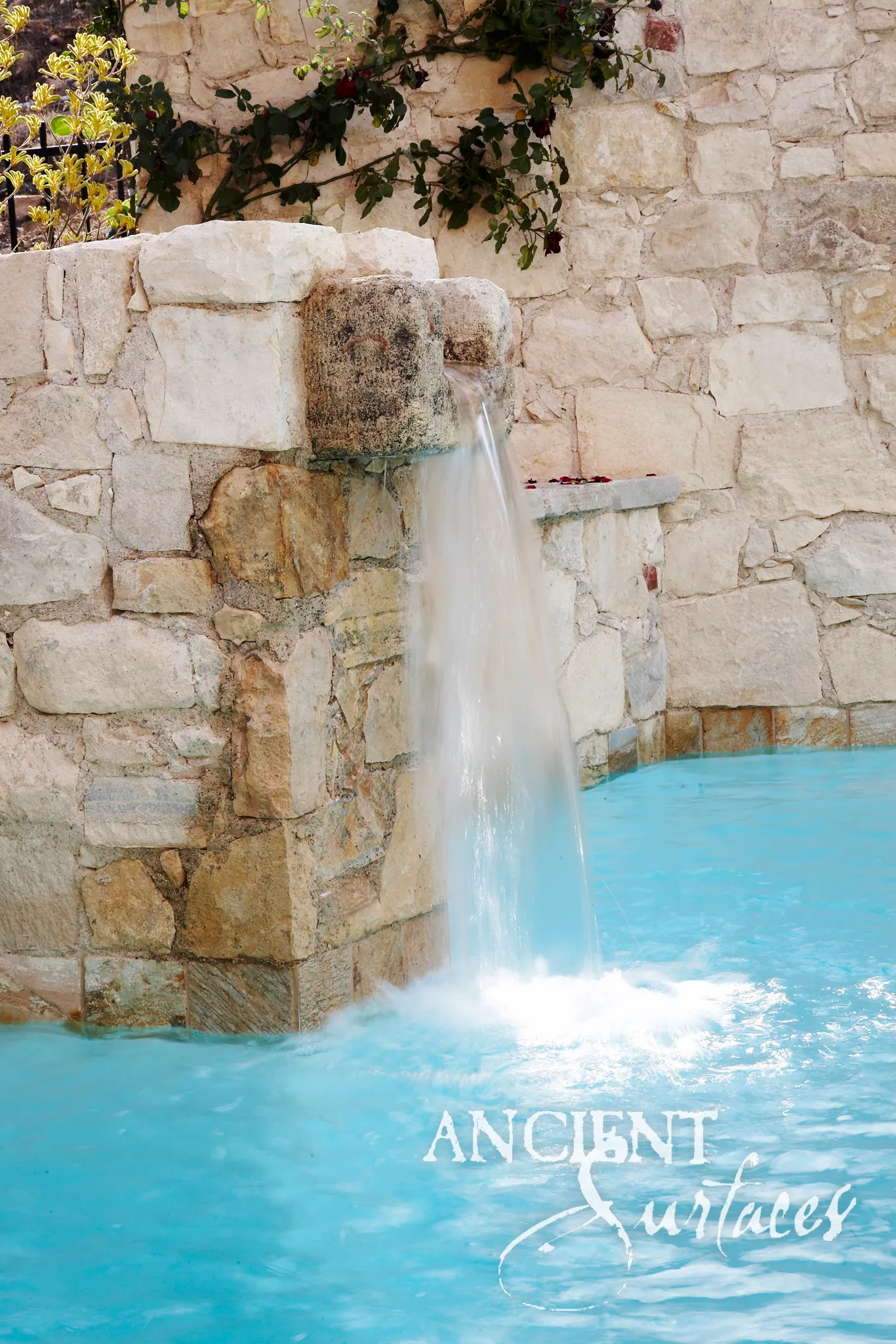 Reclaimed antique stone spout water feature from Ancient Surfaces built into a rusticated wall, pouring water directly into a swimming pool